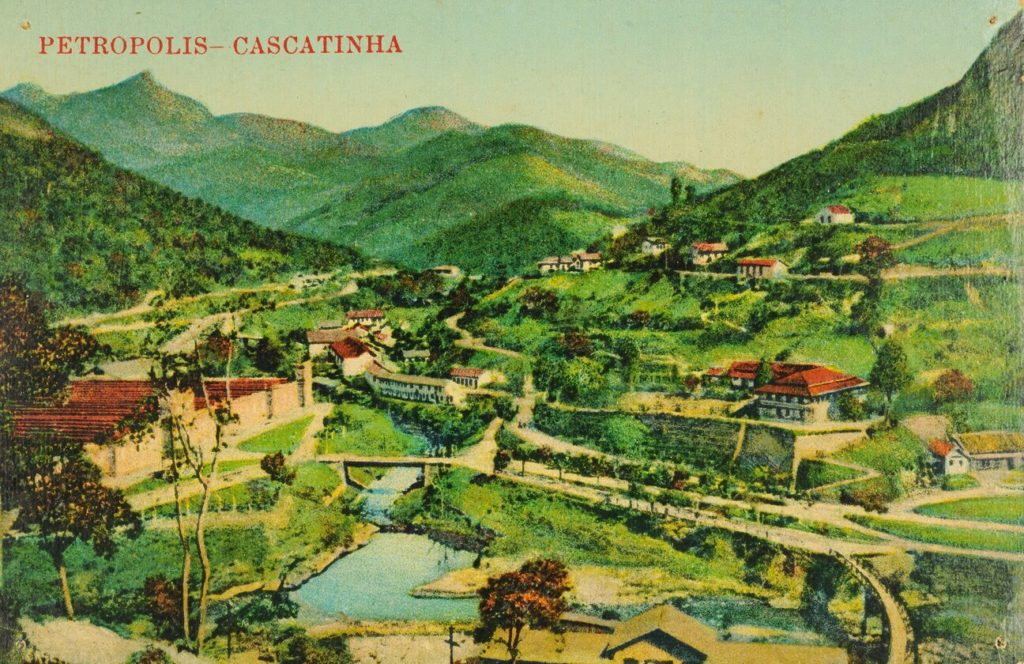 ) Cartão-postal impresso mostrando vista de parte do bairro de Cascatinha. Veem-se o rio Itamarati ao centro e a Companhia Petropolitana de Tecidos à esquerda.