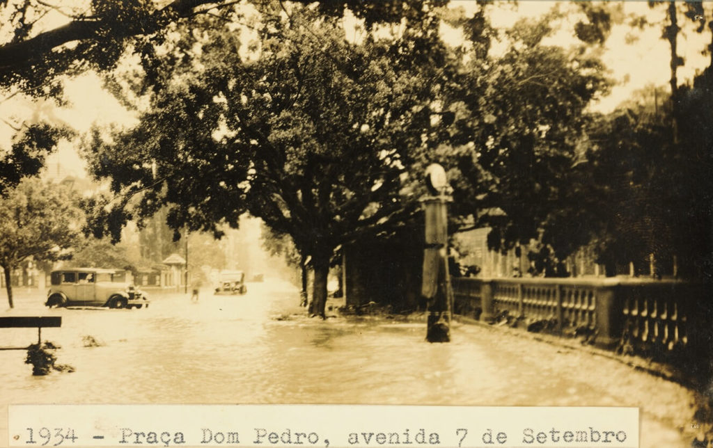 1934 - inundação nas imediações da praça Dom Pedro e da avenida Sete de Setembro, atual rua da Imperatriz. Veem-se alguns automóveis parados por causa do excesso de água e, em frente à praça, vê-se uma bomba de gasolina.